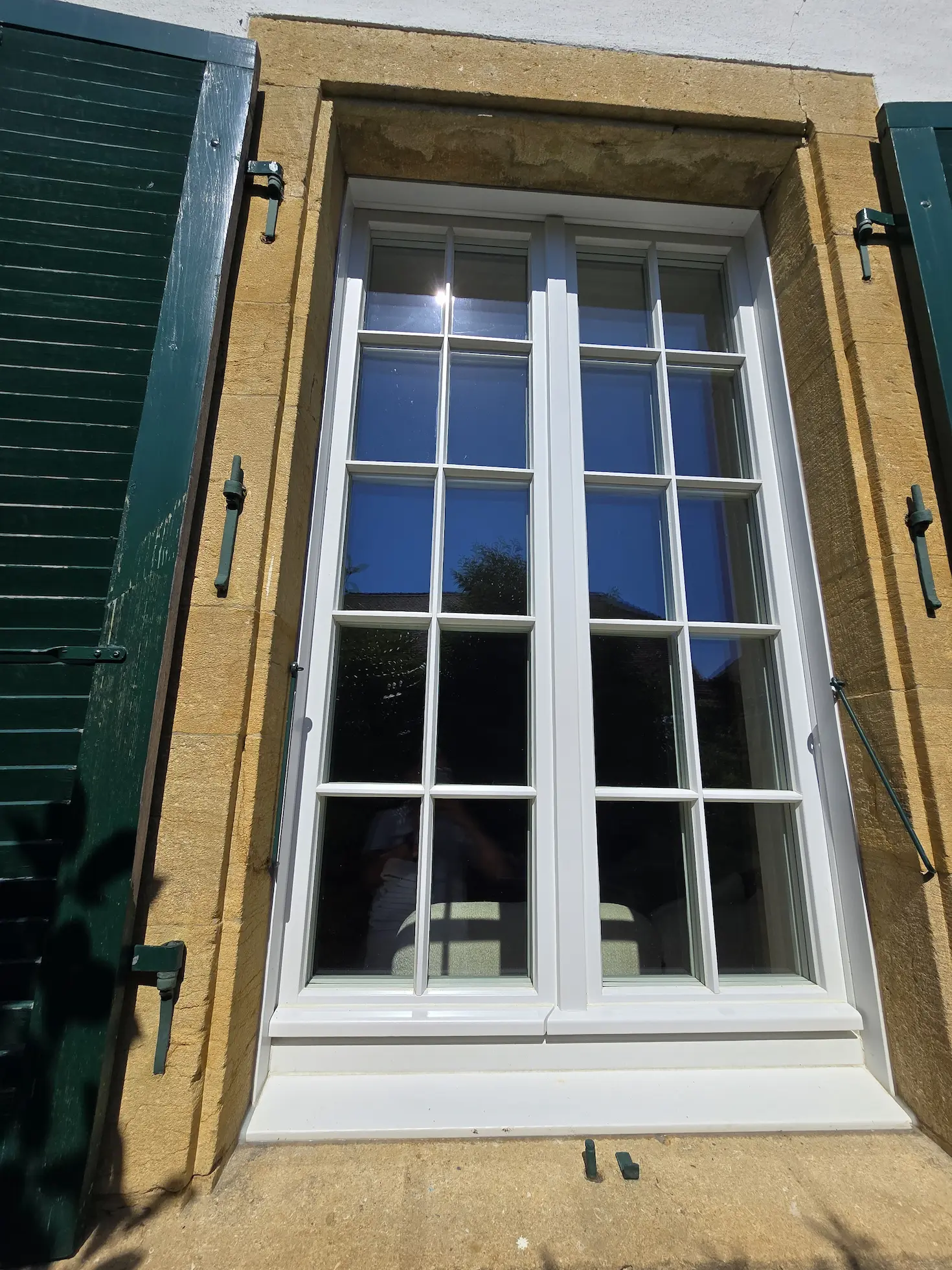 Weisses Sprossenfenster in einer Steineinfassung mit grünen Fensterläden
