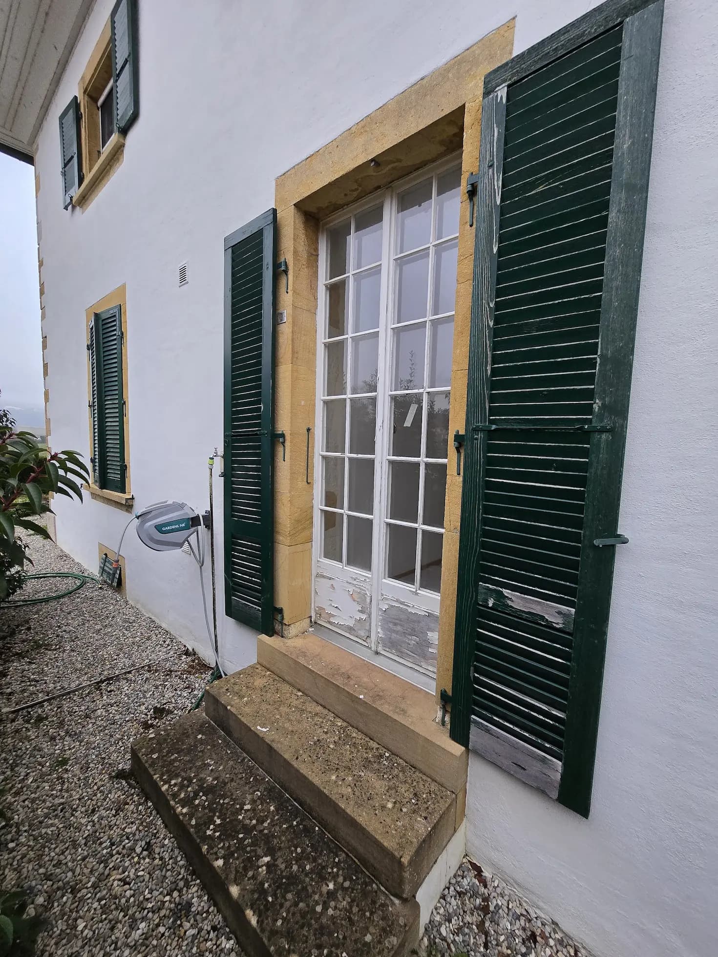 Old terrace door with peeling paint and green shutters
